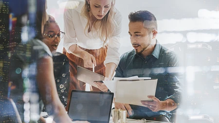 Team in moderner Büroumgebung arbeitet mit Tablet und Laptop, überlagert von urbanen Lichtreflexionen als Symbol für digitale Transformation der Arbeitswelt.