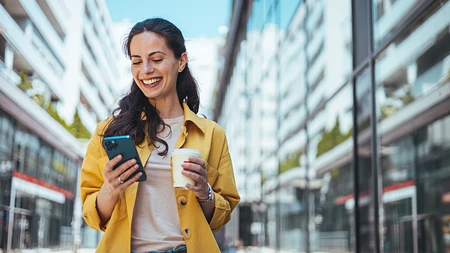 Frau mit Smartphone vor einem modernen Gebäude in der Stadt.