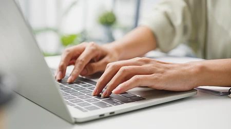 Nahaufnahme von Händen, die auf einer Laptop-Tastatur tippen.