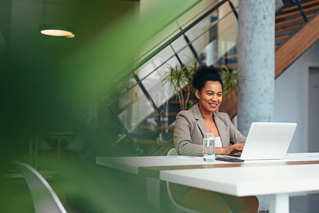 Lächelnde Frau in Businesskleidung am Laptop in modernem Büro