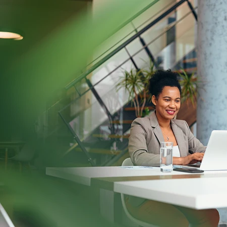 Lächelnde Frau in Businesskleidung am Laptop in modernem Büro