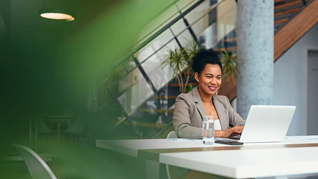 Lächelnde Frau in Businesskleidung am Laptop in modernem Büro