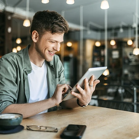 Lachender Mann in grünem Hemd, der an einem Tablet in einem Café liest