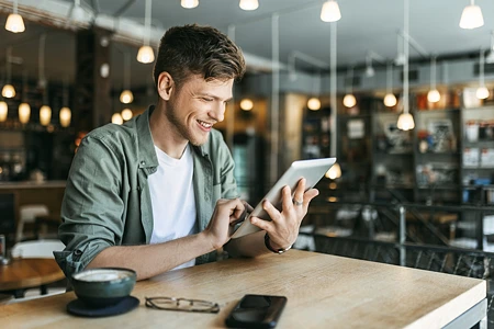 Lachender Mann in grünem Hemd, der an einem Tablet in einem Café liest