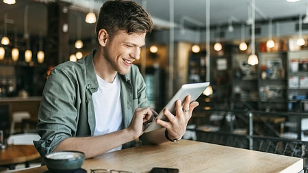 Lachender Mann in grünem Hemd, der an einem Tablet in einem Café liest
