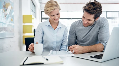 Mann und Frau besprechen Dokumente an einem Tisch mit Laptop