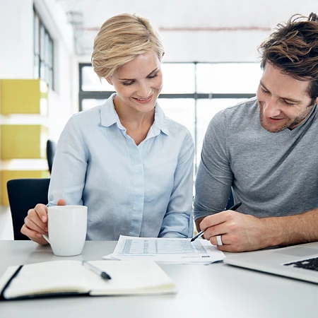 Mann und Frau besprechen Dokumente an einem Tisch mit Laptop