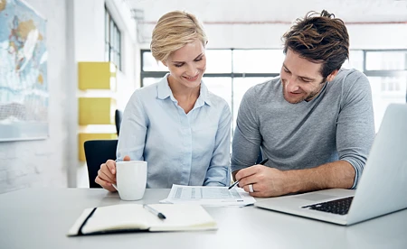 Mann und Frau besprechen Dokumente an einem Tisch mit Laptop