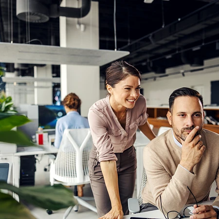 Frau und Mann in Business-Kleidung schauen gemeinsam auf einen Monitor in einem modernen Büro.