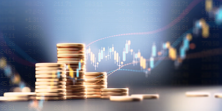 Stapel von Goldmünzen vor einem Hintergrund mit blauem Börsenchart und Finanzdaten.