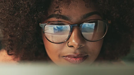 Nahaufnahme einer Frau mit Brille, in deren Gläsern ein Computerbildschirm reflektiert wird: Genau hinsehen lohnt sich!