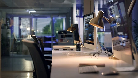 Leeres Großraumbüro bei Nacht, auf einem Schreibtisch leuchtet ein Monitor mit einem Daten-Dashboard, die Stühle davor sind unbesetzt.