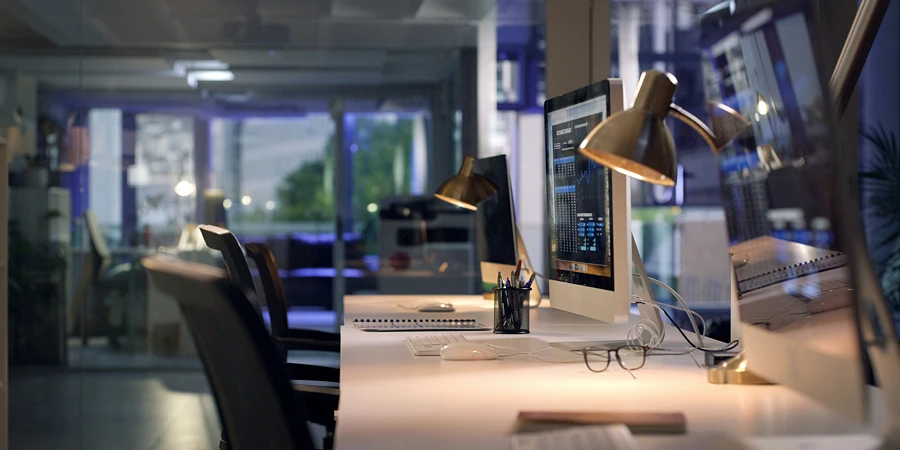 Leeres Großraumbüro bei Nacht, auf einem Schreibtisch leuchtet ein Monitor mit einem Daten-Dashboard, die Stühle davor sind unbesetzt.