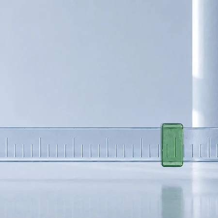 Ein transparentes Lineal mit einem grünen Markierungsschieber auf einer glänzenden weißen Fläche.